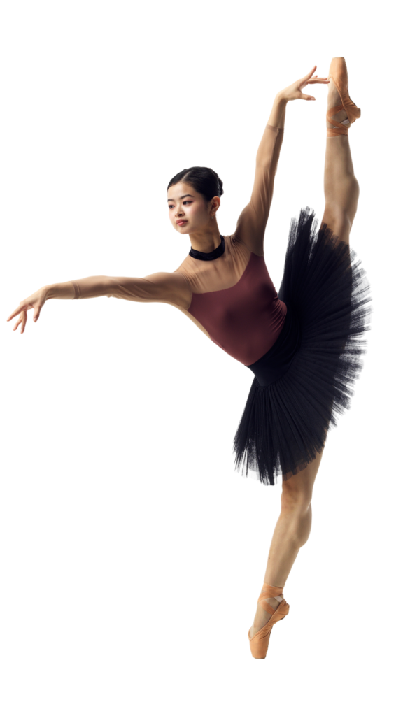 A ballerina in a burgundy leotard and black tutu performs an elegant arabesque on pointe against a white background. Her expression is focused and poised.